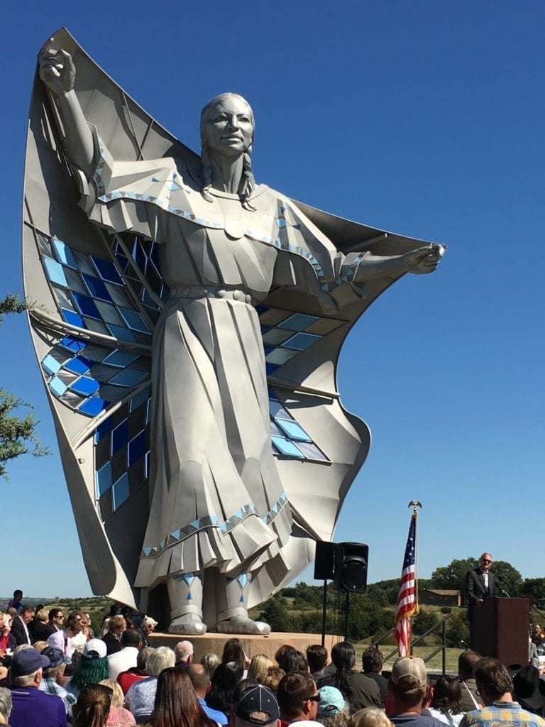 Statue of a native american person holding a diamond quilt over their shoulders